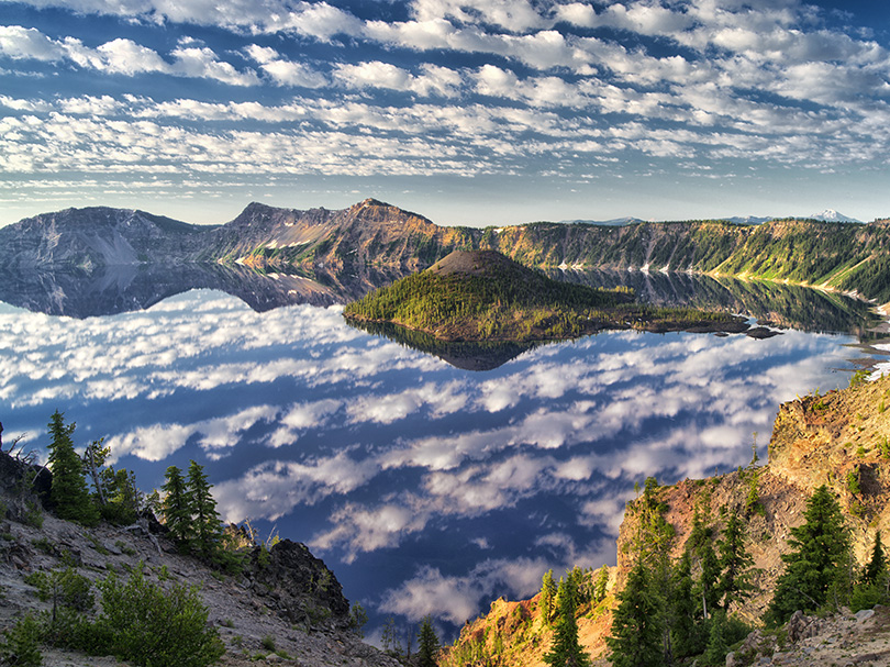 I have photographed Crater Lake many times in all seasons over the last 25 years, but this day was the most special. On a four day photo trip with a fellow photographer, we spent every morning and evening at the lake’s rim waiting for something special to happen with the sky/lighting as we have done on so many occasions. We saw a scant few clouds forming this particular morning, but were pleasantly surprised when the entire sky was soon covered in these beautiful “popcorn” clouds. An added bonus was the absolute calmest conditions I have ever seen at the lake, which by the way, didn’t help with the mosquitoes! They were eating us alive, but we hardly noticed as we shot from a variety of locations for almost an hour before the clouds totally disappeared. I know my family would have bailed on this scene because of the conditions, and I can’t blame them.