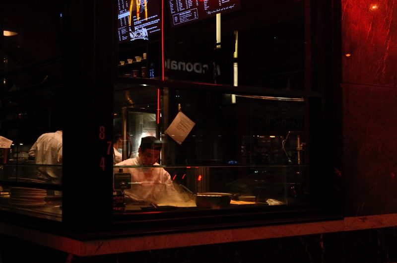 An asian man makes a crepe in a shop window.