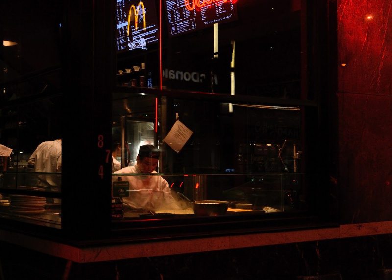 An asian man makes a crepe in a shop window.