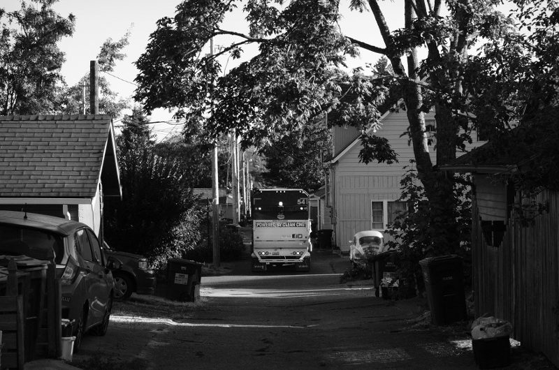 The back end of a garbage truck, exiting one alley, heading into the next