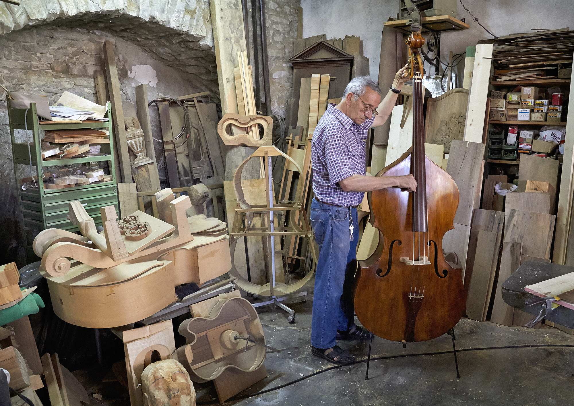 A man tunes a chello in his Instrument workshop while surronded by thin pieces of wood that shape the skeleton of other instruments.