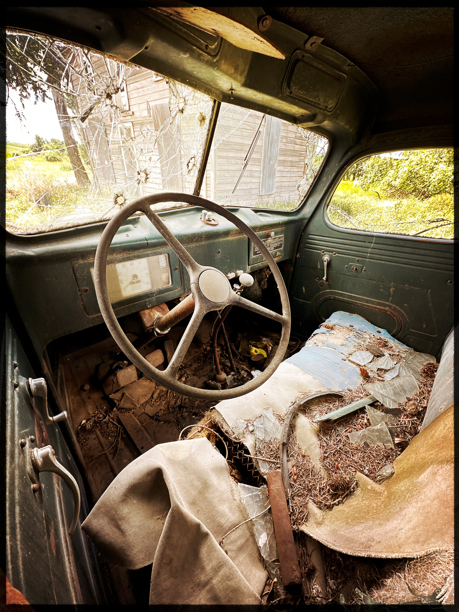 Looking at an abandoned house through and abandoned truck