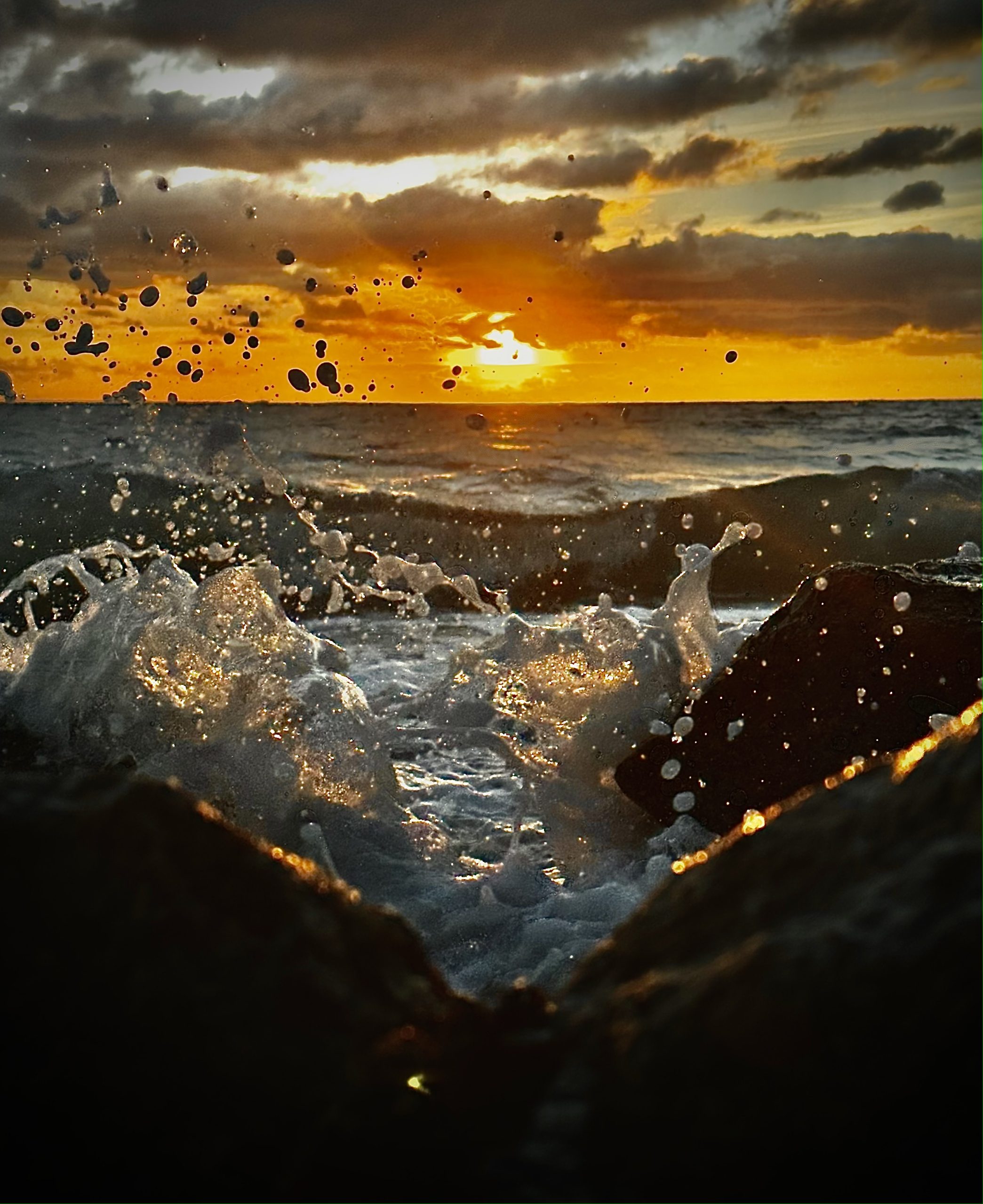 frozen image of water lapping over the rocks of the beach, with the sun setting behind it.