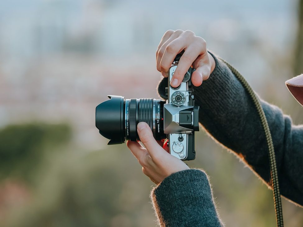 Close-up of a photographer adjusting camera settings on a mirrorless camera with a professional lens, preparing for an outdoor photoshoot.