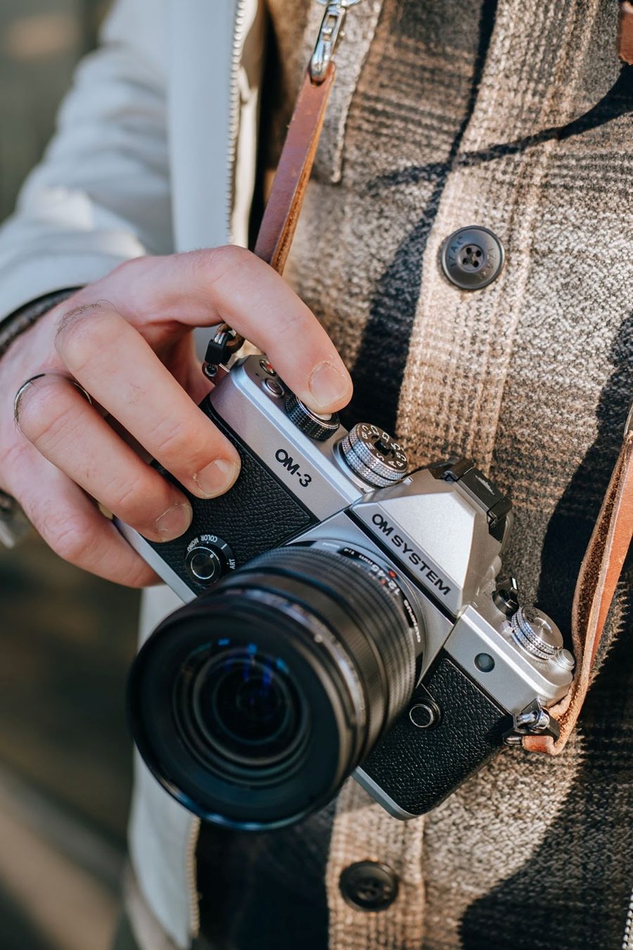 Photographer holding an OM System OM-3 mirrorless camera with a zoom lens, ready for an outdoor photoshoot. Ideal gear for professional and enthusiast photographers.
