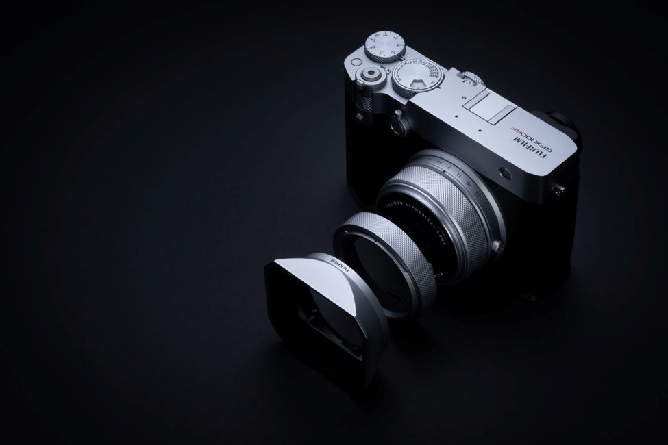 Fujifilm GFX100RF medium format camera in silver, showcased with its GF lens and detached metal lens hood. A high-end mirrorless camera blending retro design with modern photography innovation.