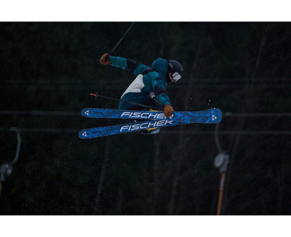 Freestyle skier performing a mid-air grab on Fischer skis, captured in low-light conditions with the Sigma 300-600mm f/4 DG OS Sports lens, showcasing its fast autofocus and sharp image quality for action sports photography.