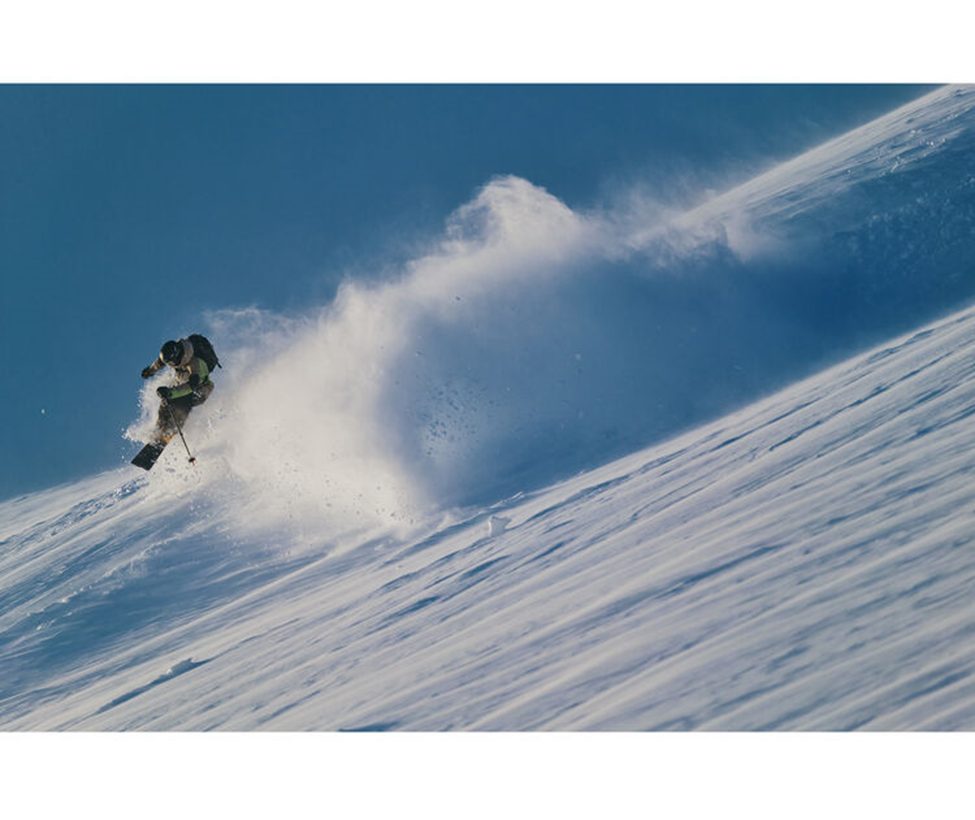 Skier carving through fresh powder on a steep slope, with a dramatic snow spray captured using the Sigma 300-600mm f/4 DG OS Sports lens, highlighting its sharpness and fast autofocus for dynamic winter sports photography.