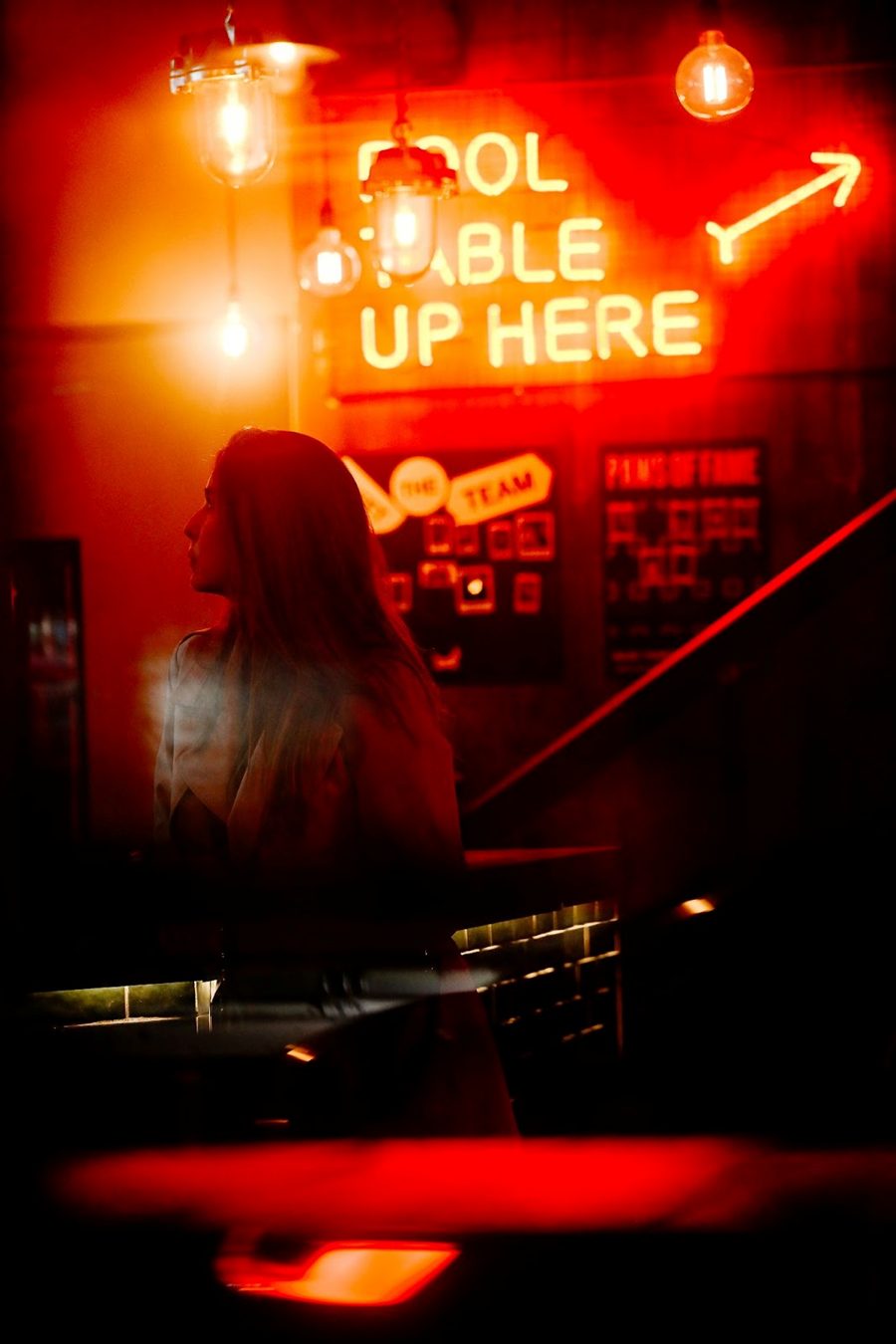Moody neon-lit bar scene: A woman gazes into the distance, illuminated by red neon lights, showcasing the low-light capabilities of modern cameras like the Nikon Z5 II