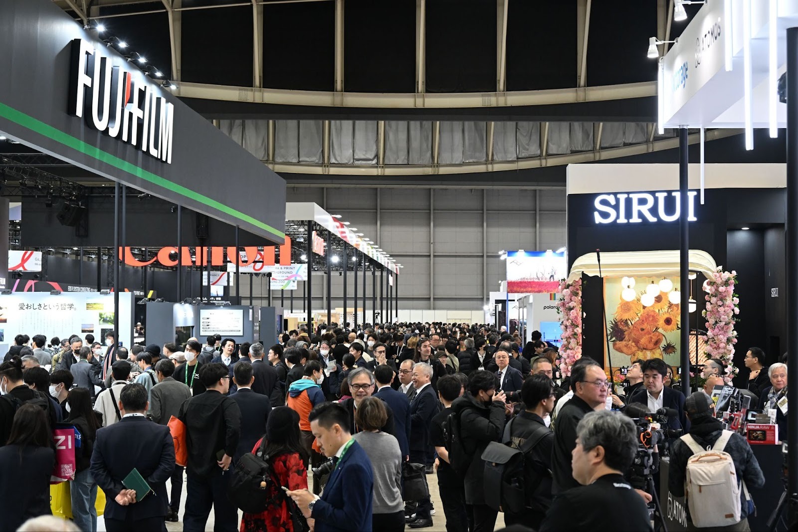 Crowded CP+ exhibition hall with Fujifilm and Sirui booths and attendees exploring gear