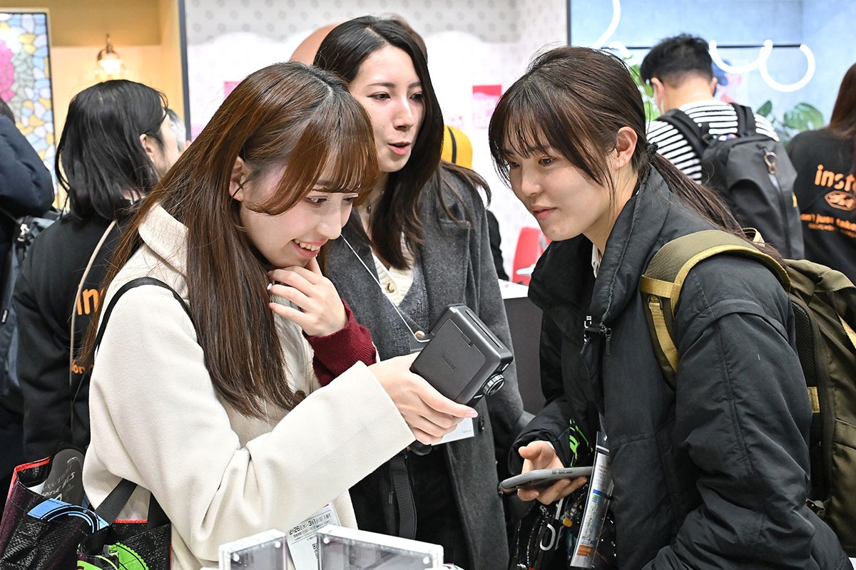 Visitors examining an Instax camera at the Fujifilm booth