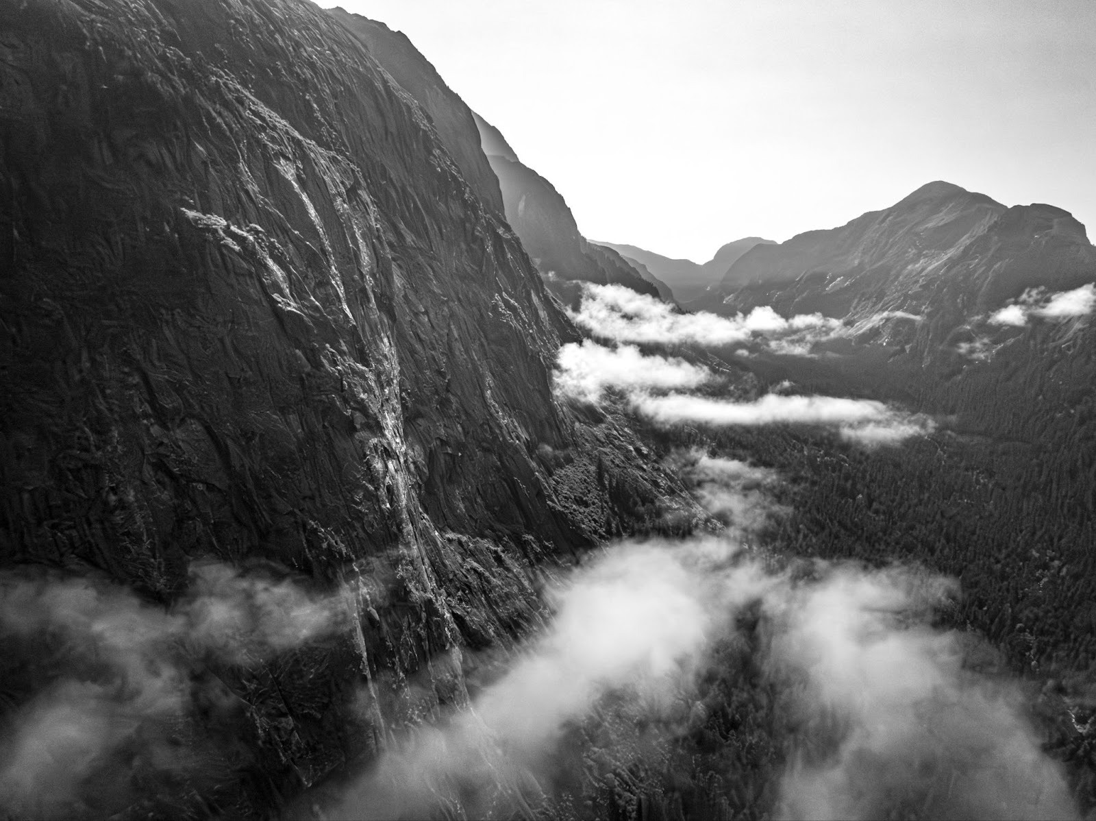 Black and white mountain valley with clouds drifting between cliffs