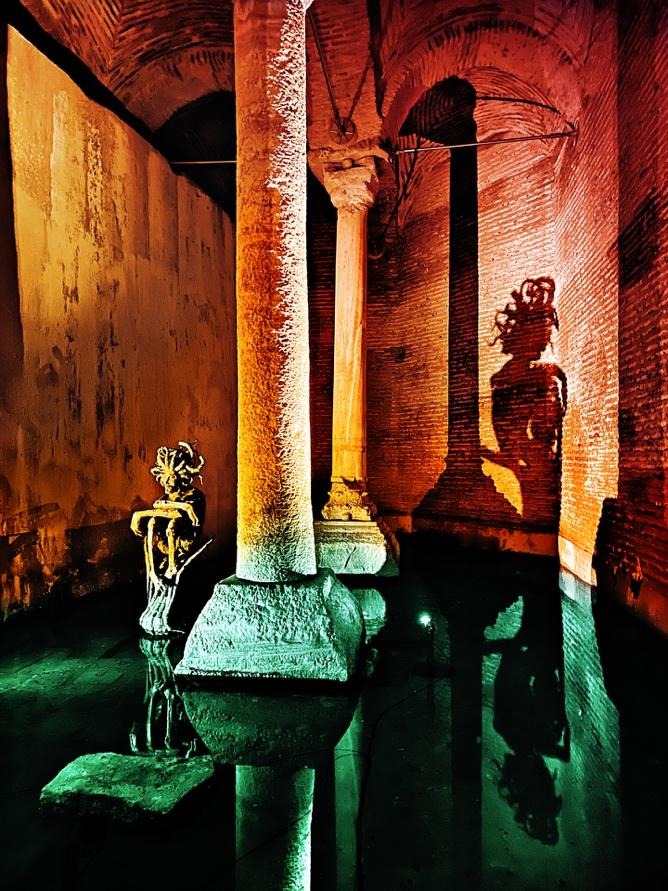 Medusa sculpture casting shadow on cistern wall with green-lit water