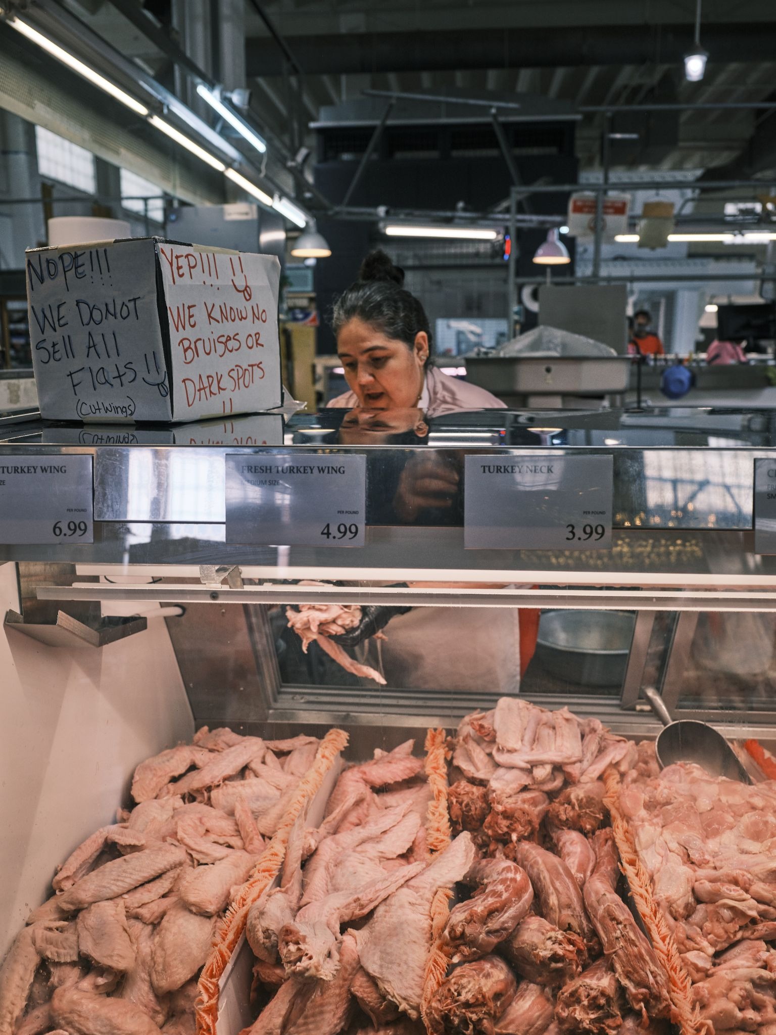 Vendor behind poultry counter in indoor market, demonstrating GFX100RF documentary detail