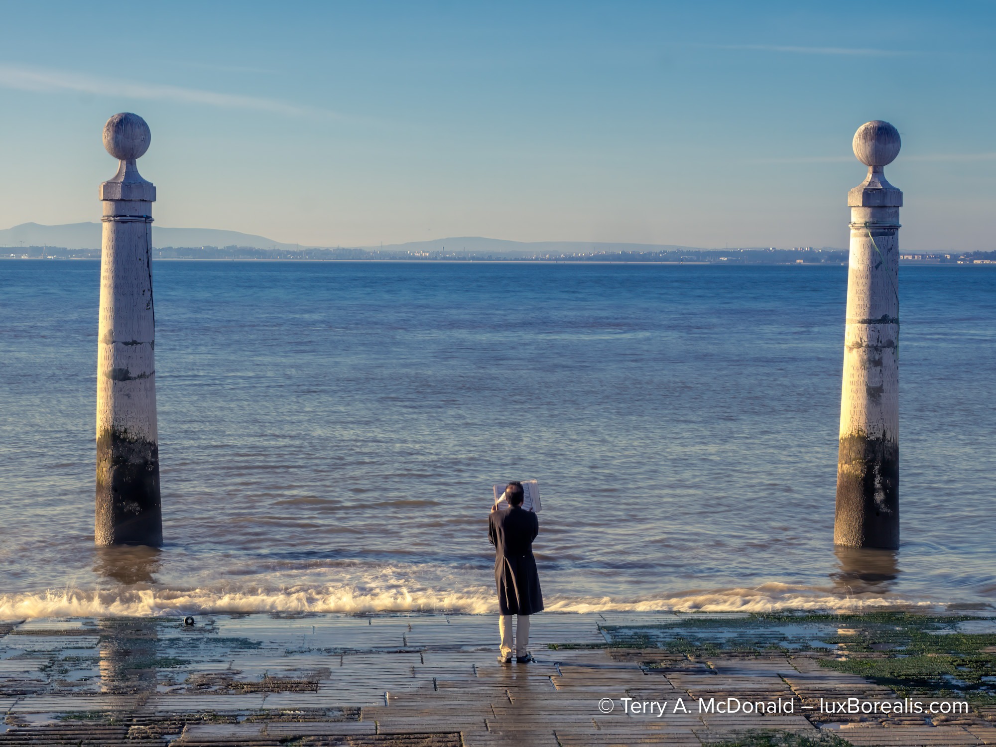 Person reading by the Tagus River between two stone pillars in Lisbon