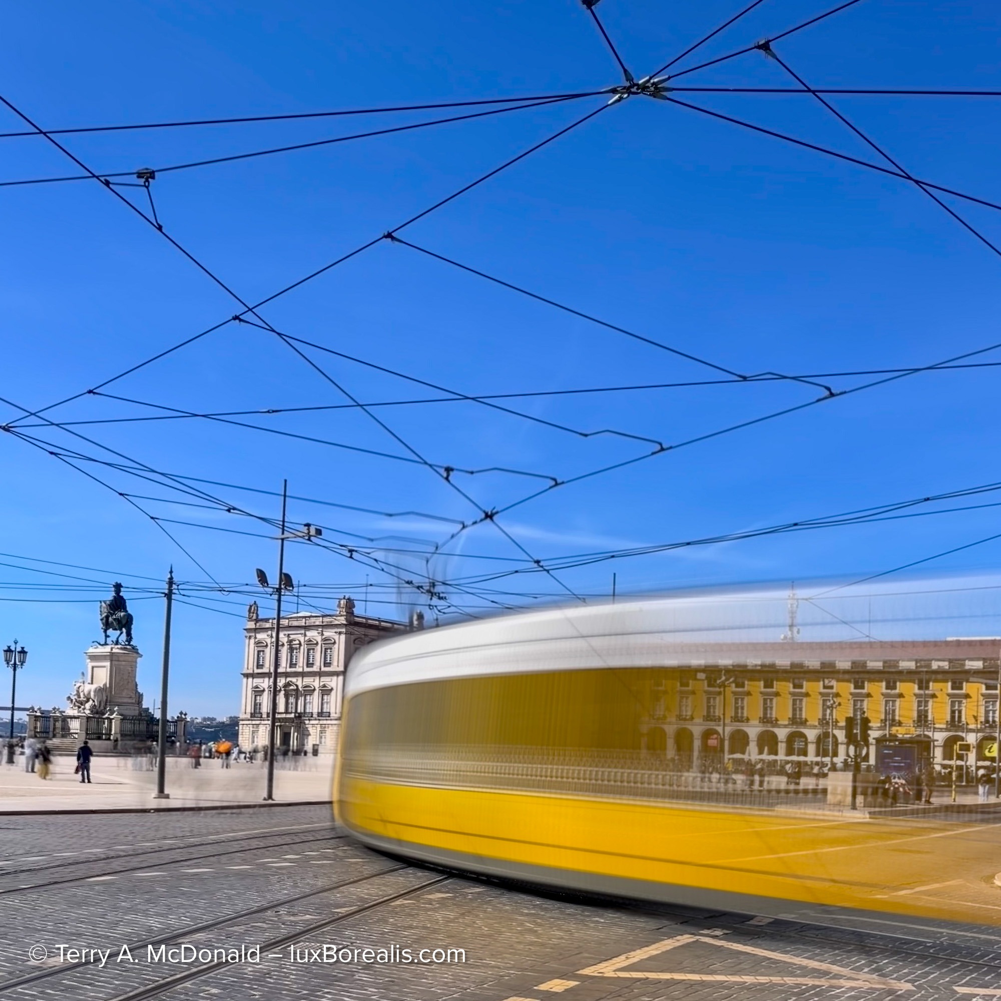 Yellow Lisbon tram blurred in motion across Praça do Comércio