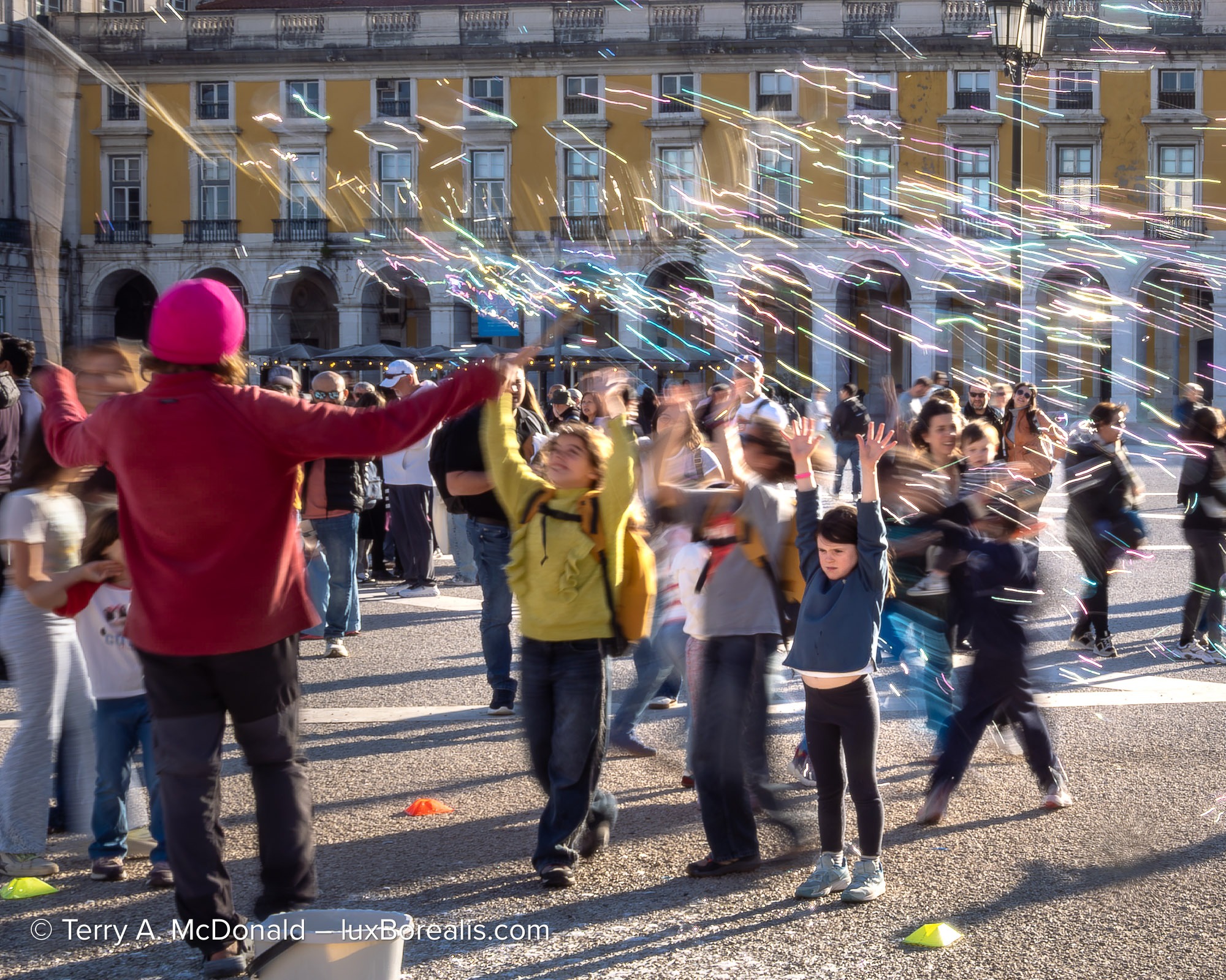 Children reaching for bubbles in Praça do Comércio during a street performance