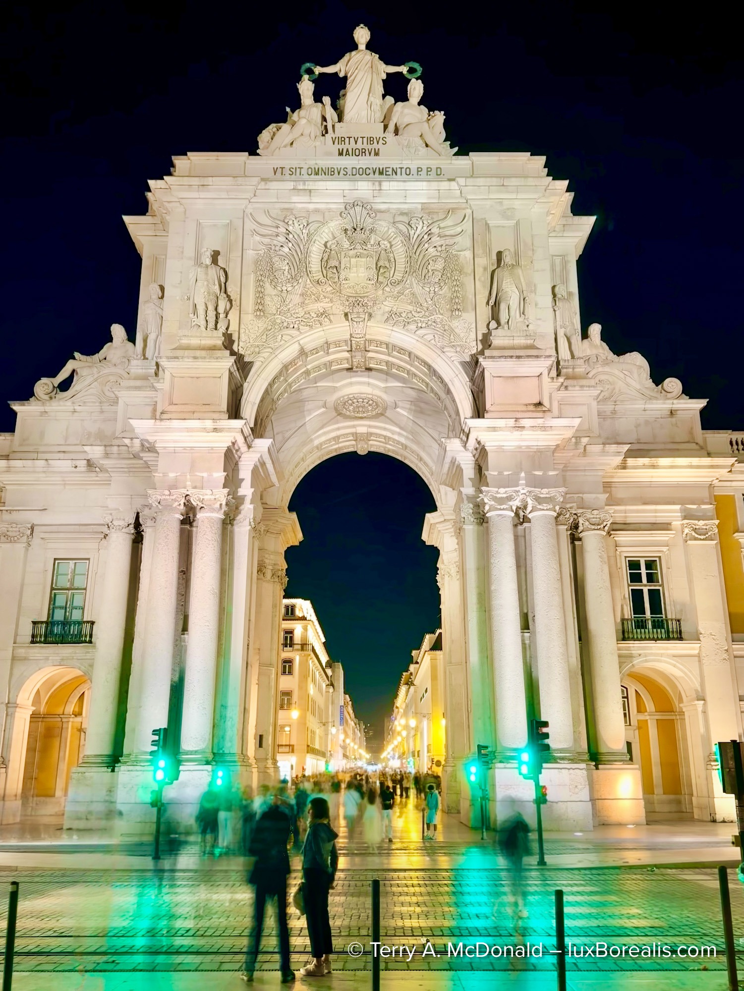 Rua Augusta Arch illuminated at night with blurred pedestrians below