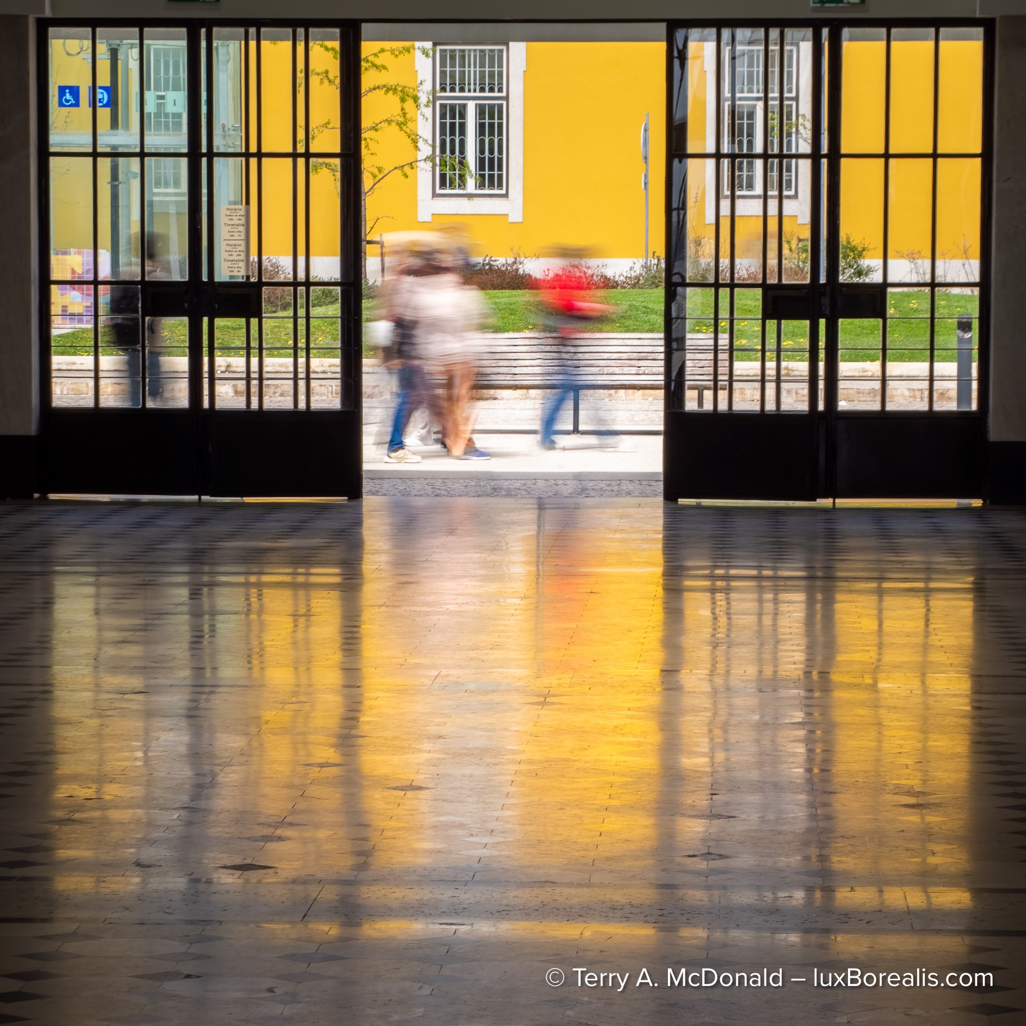 Blurred pedestrians framed by open doors with reflections on a polished floor
