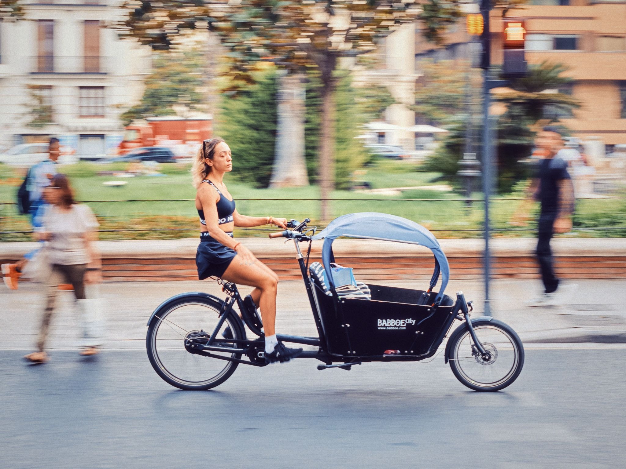 Woman riding a cargo bike through a city street with motion blur.
