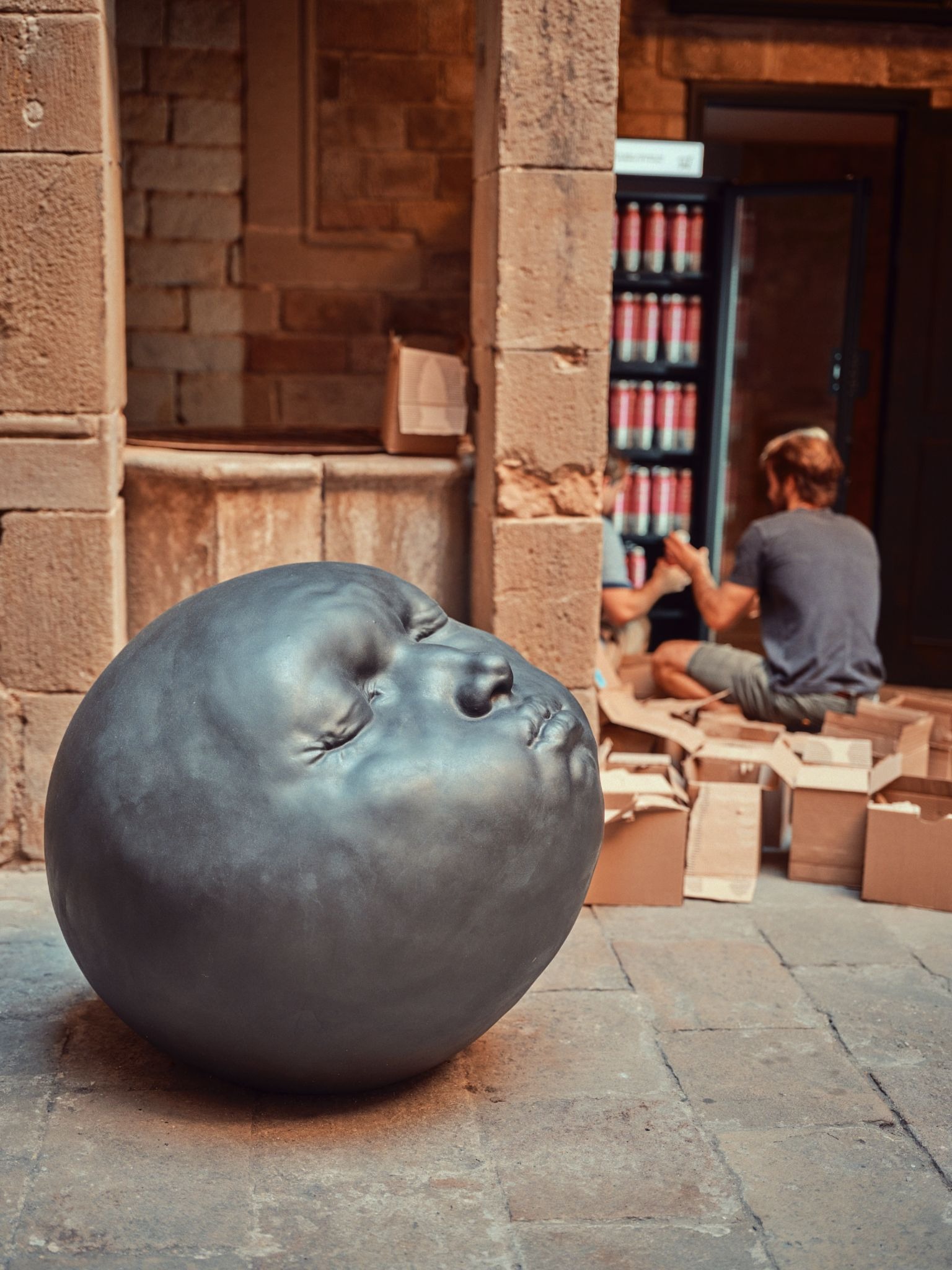 Round sculpture with a human face displayed in a courtyard.