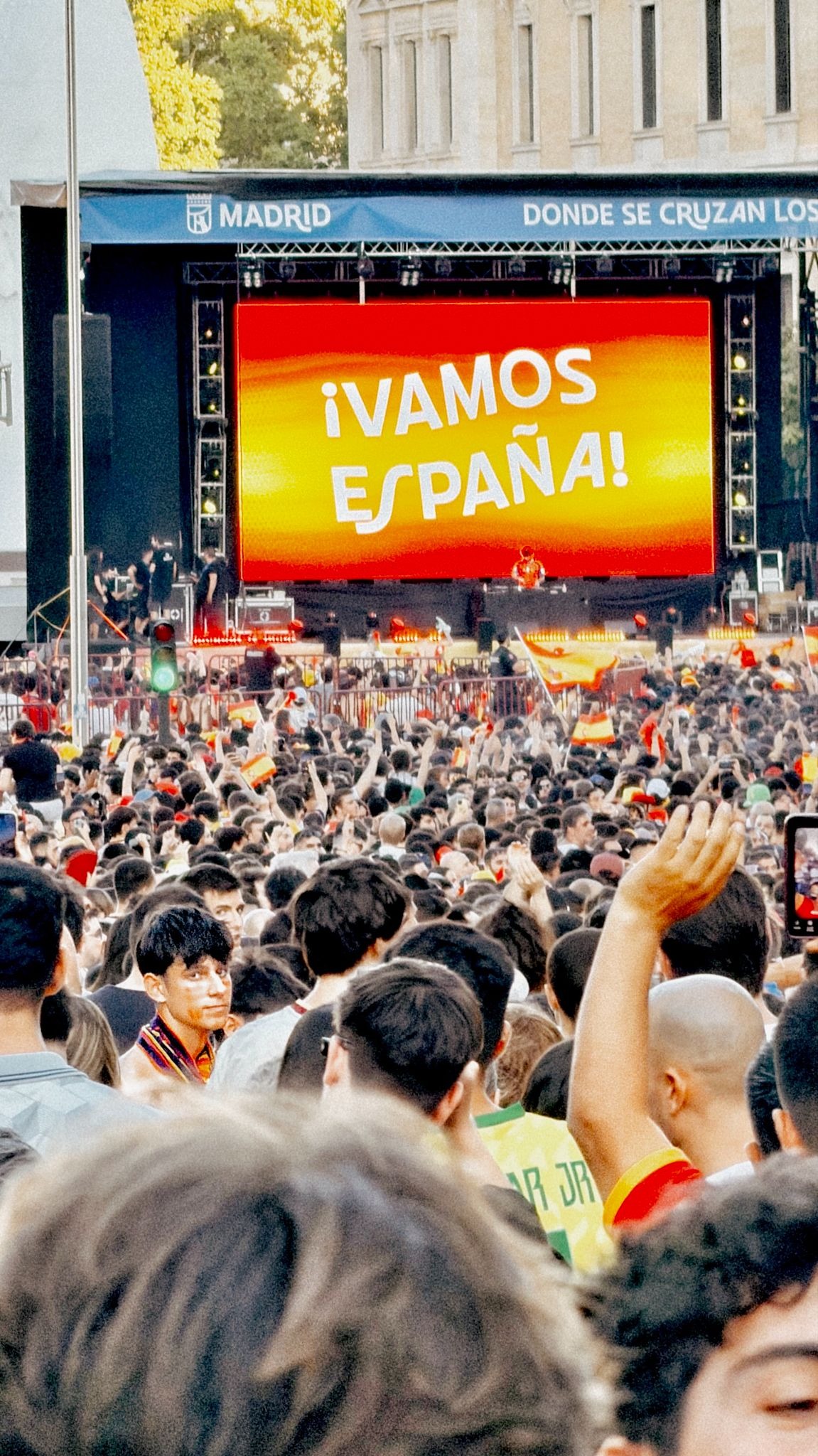 Crowd gathered in Madrid beneath a giant "¡Vamos España!" screen.