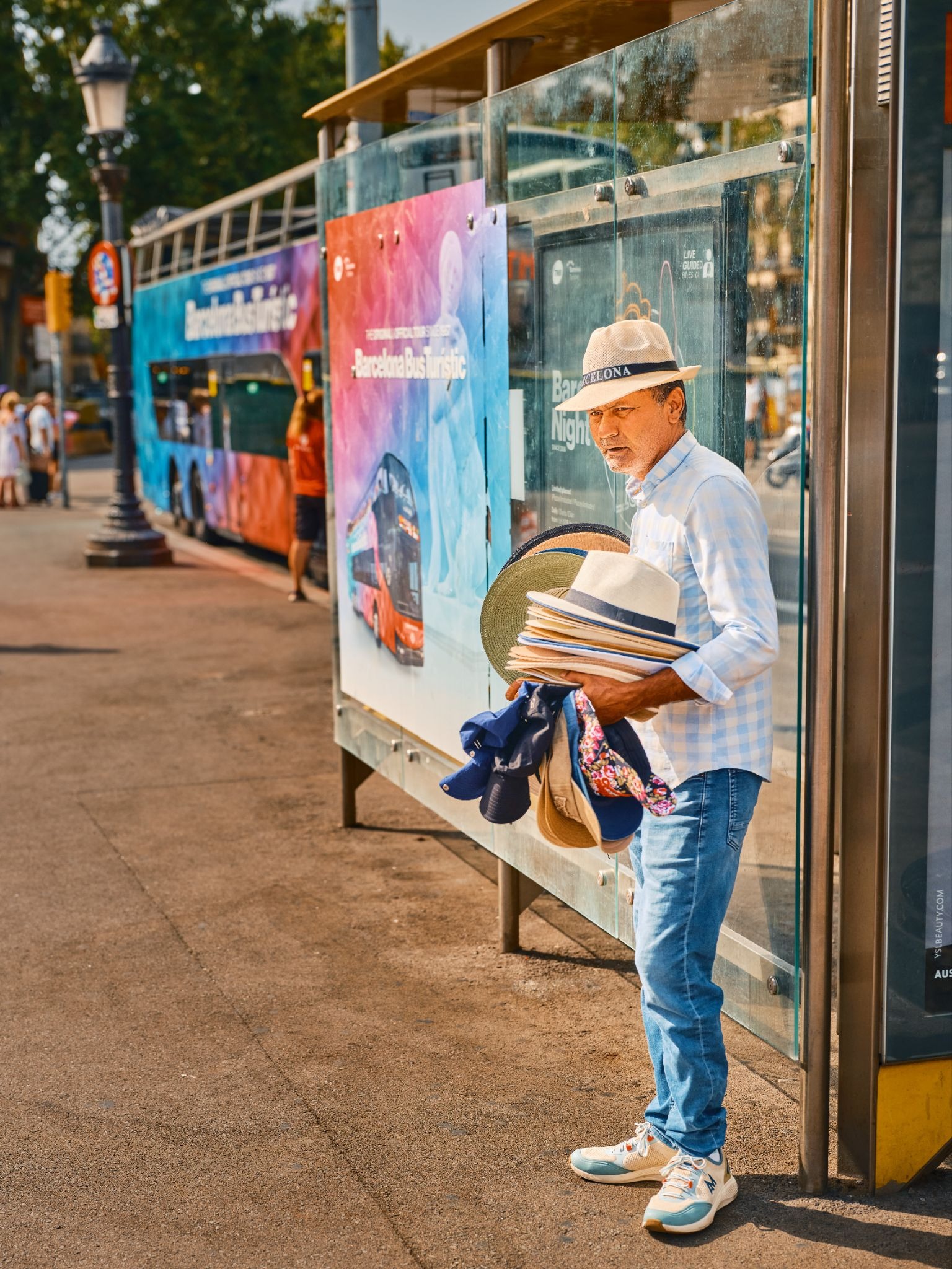 Hat vendor standing at a Barcelona bus stop with stacked hats.
