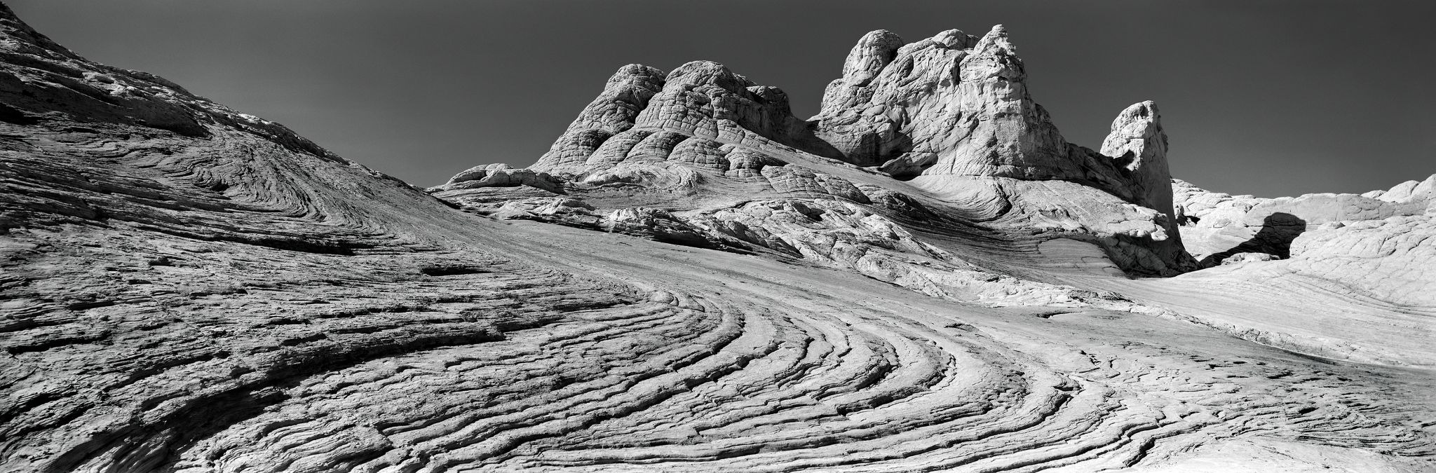 Layered sandstone formations under a clear sky in a panoramic black-and-white landscape