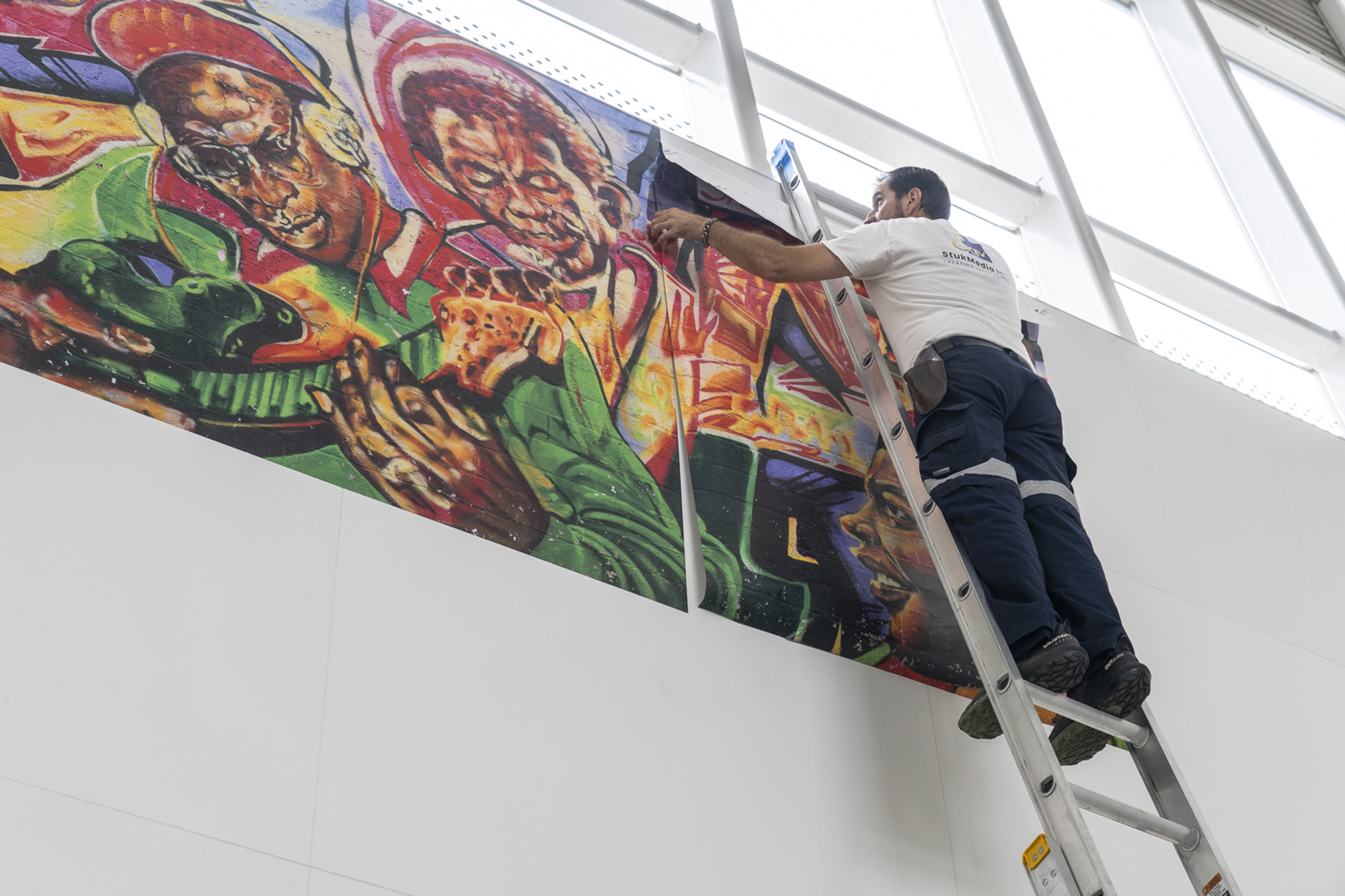 Installer aligning a Reggae mural panel on the station wall