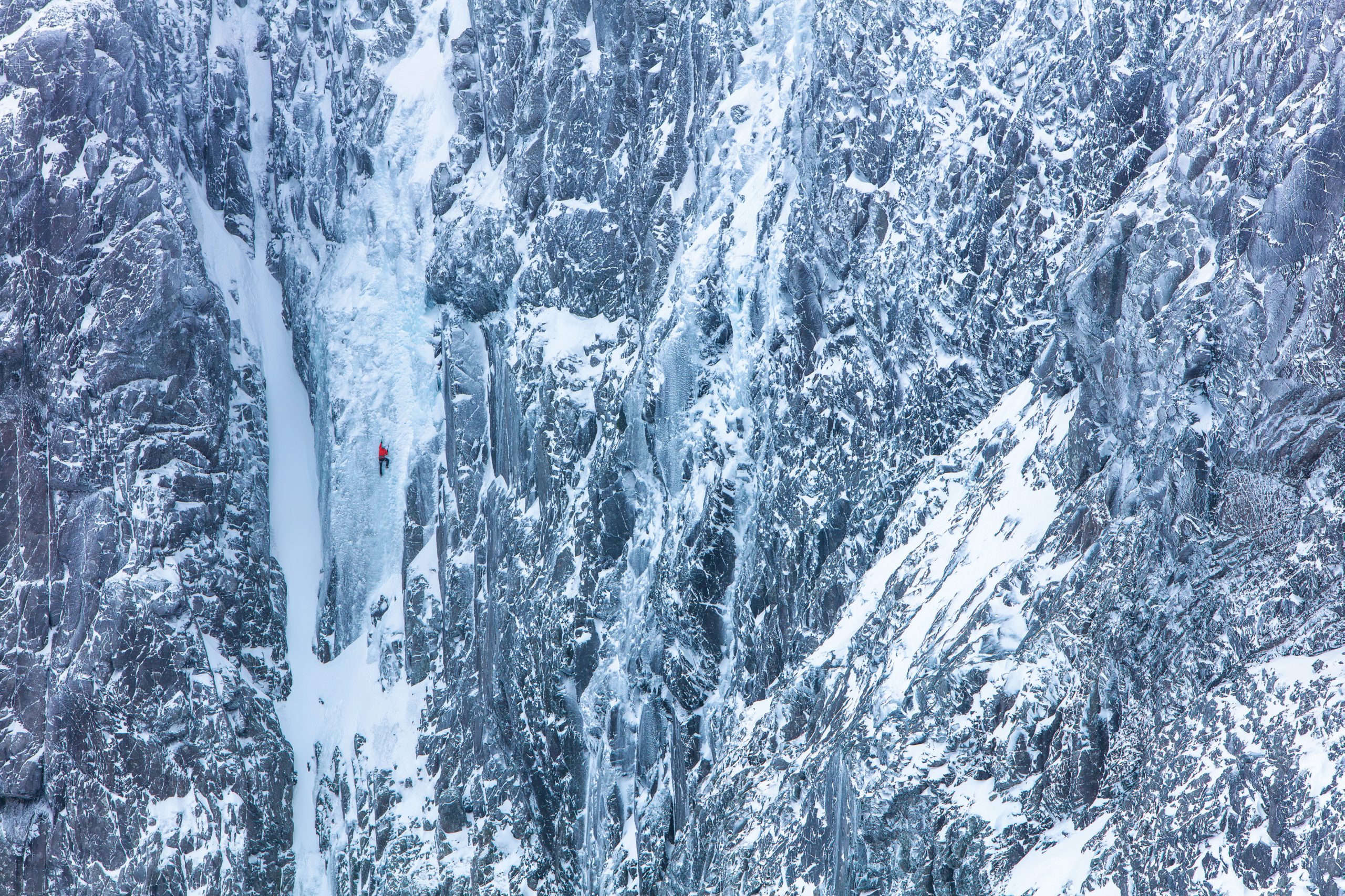 Climber ascending a steep ice-covered mountain face surrounded by snow and rock