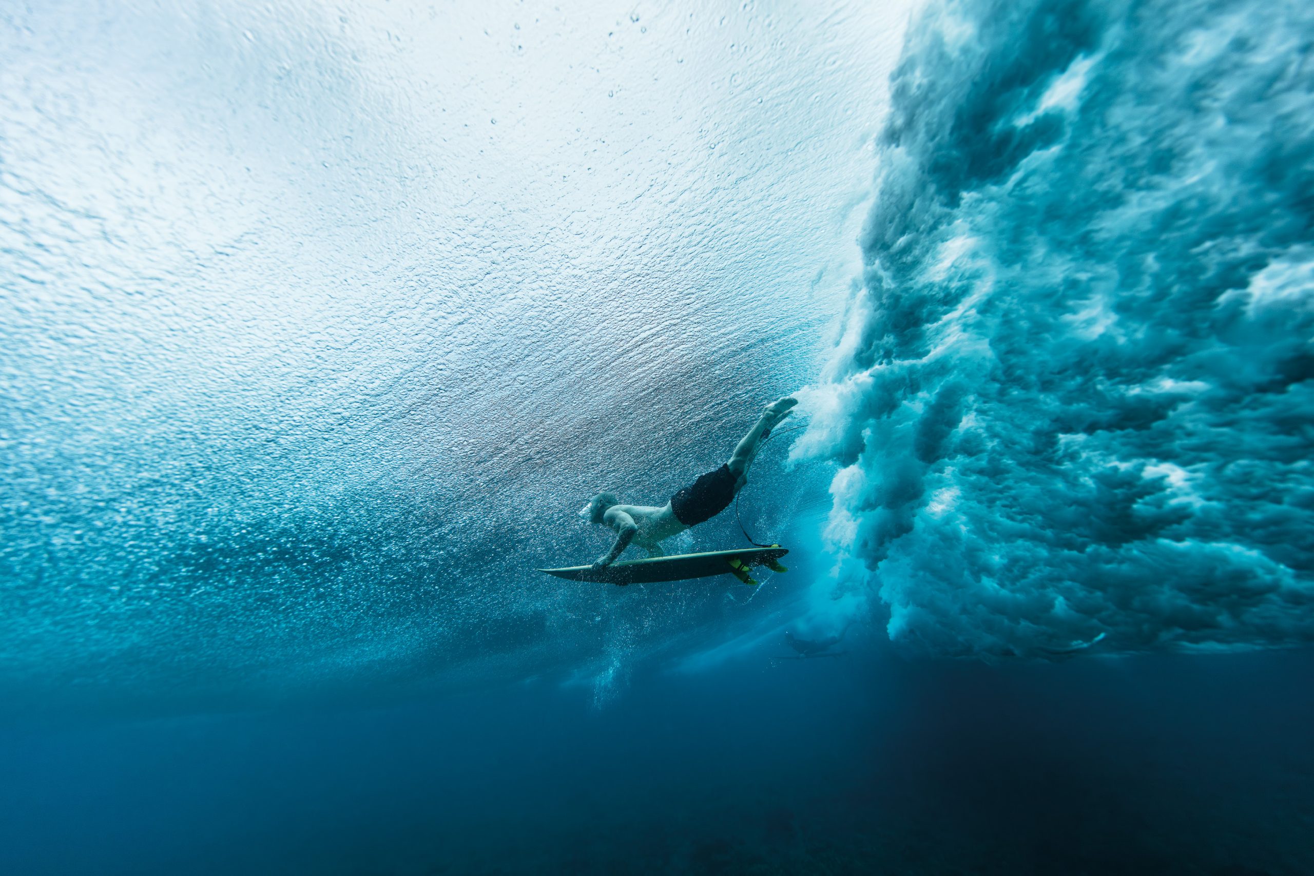 A surfer riding a surfboard underwater beneath a breaking ocean wave.