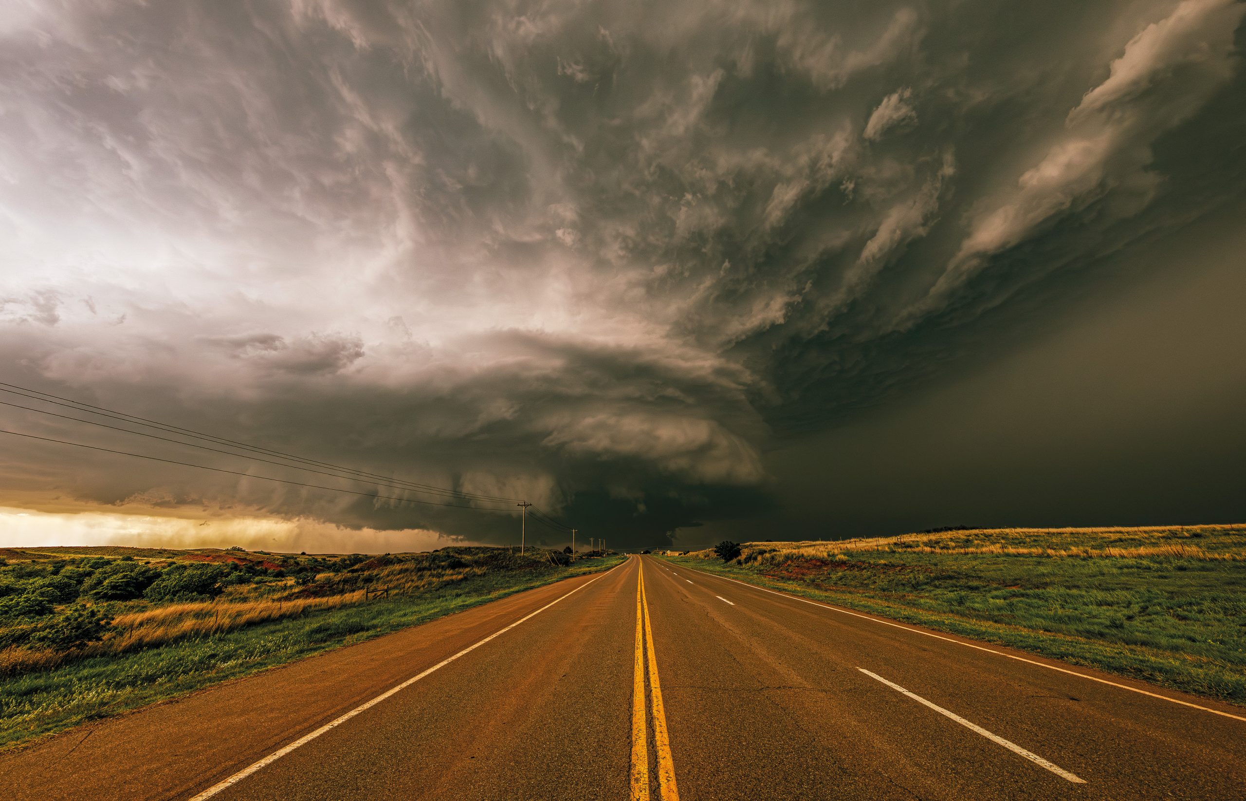 Dramatic storm clouds over a rural highway stretching across the open landscape