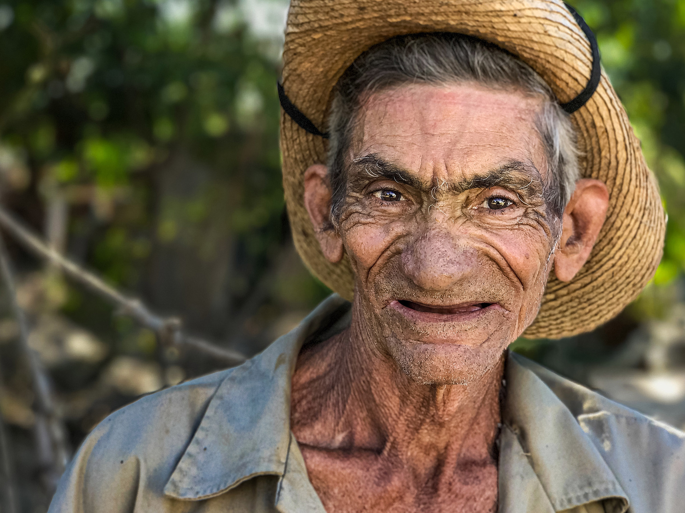 Portrait of an older Cuban man wearing a straw hat and blue shirt.