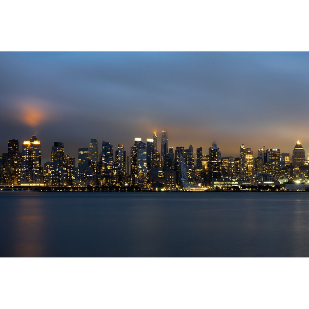 Nighttime city skyline with illuminated buildings reflected on the water.