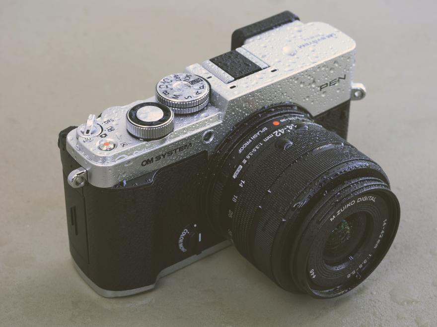 Silver OM SYSTEM PEN with 14-42mm lens in the rain