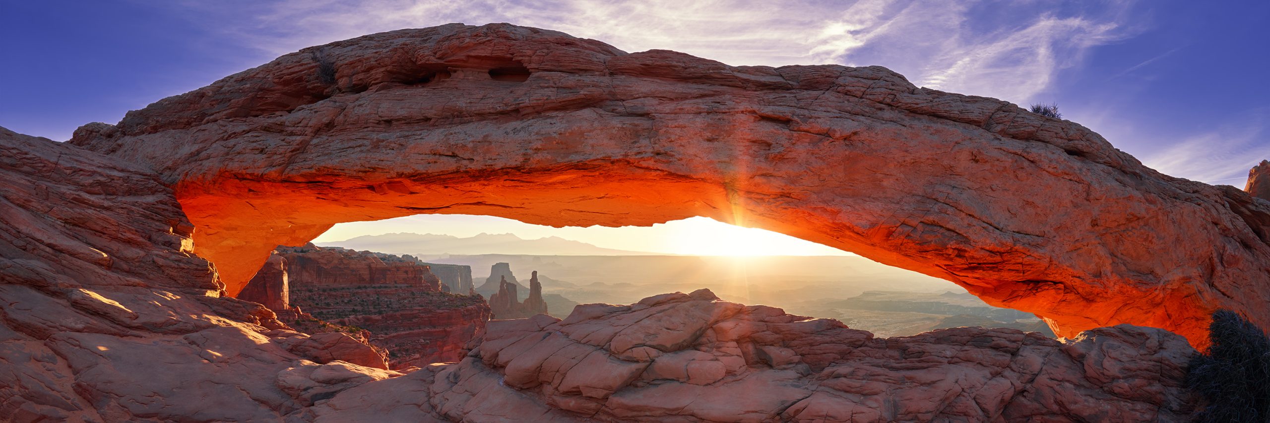 Mesa Arch framing the canyon and distant rock formations in warm light