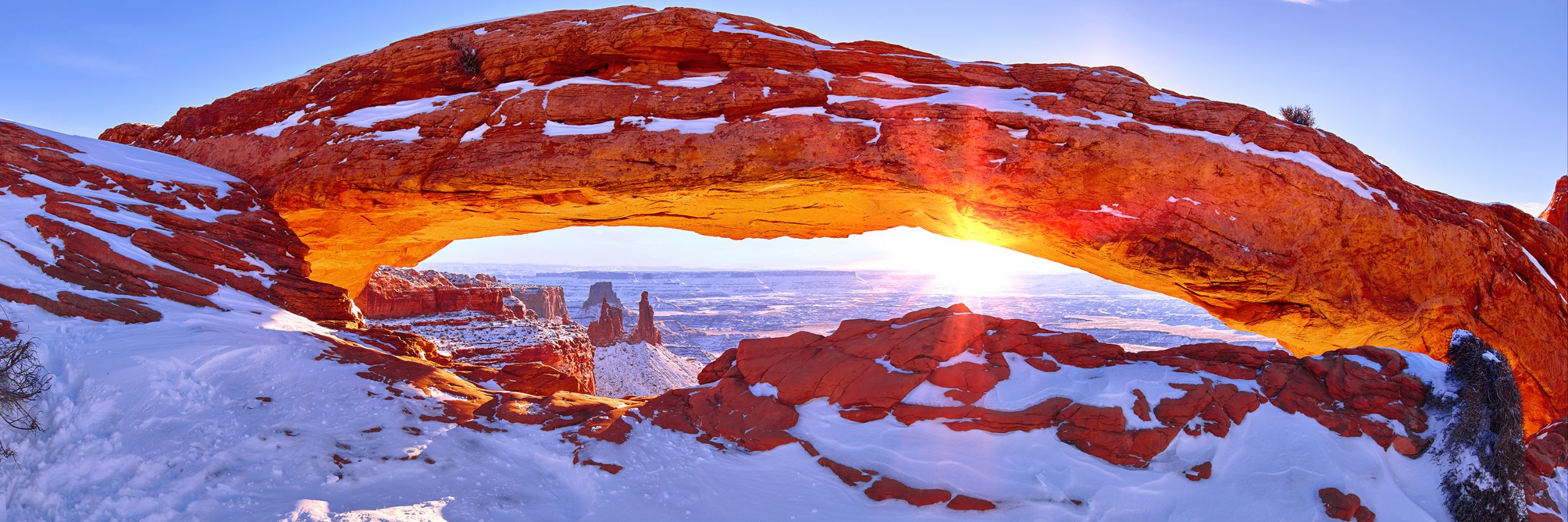 Snow-covered Mesa Arch glowing orange in the winter morning light