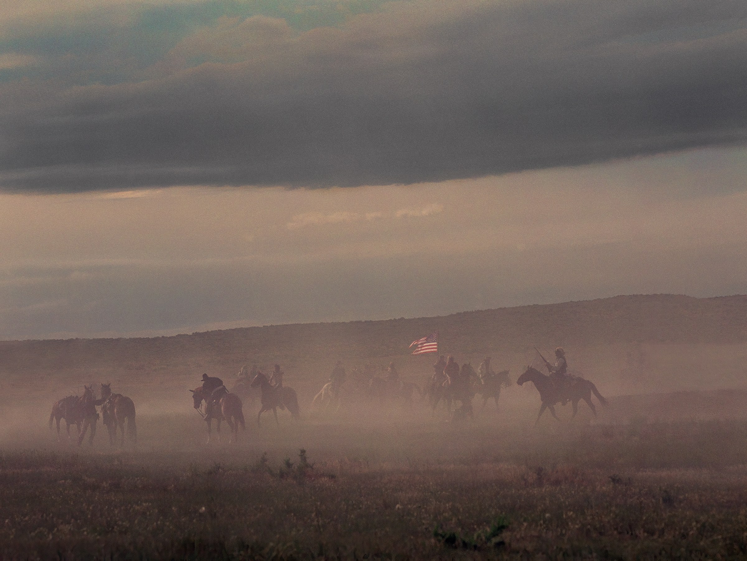 Horseback riders reenact Custer’s Last Stand across a dusty landscape beneath a dramatic sky, photographed by Stephen Wilkes.