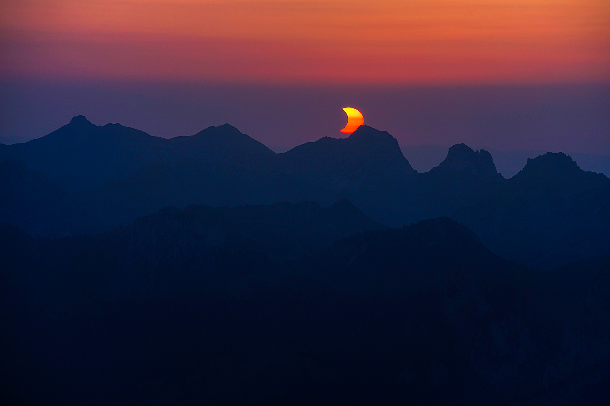 Partial solar eclipse setting behind the mountains