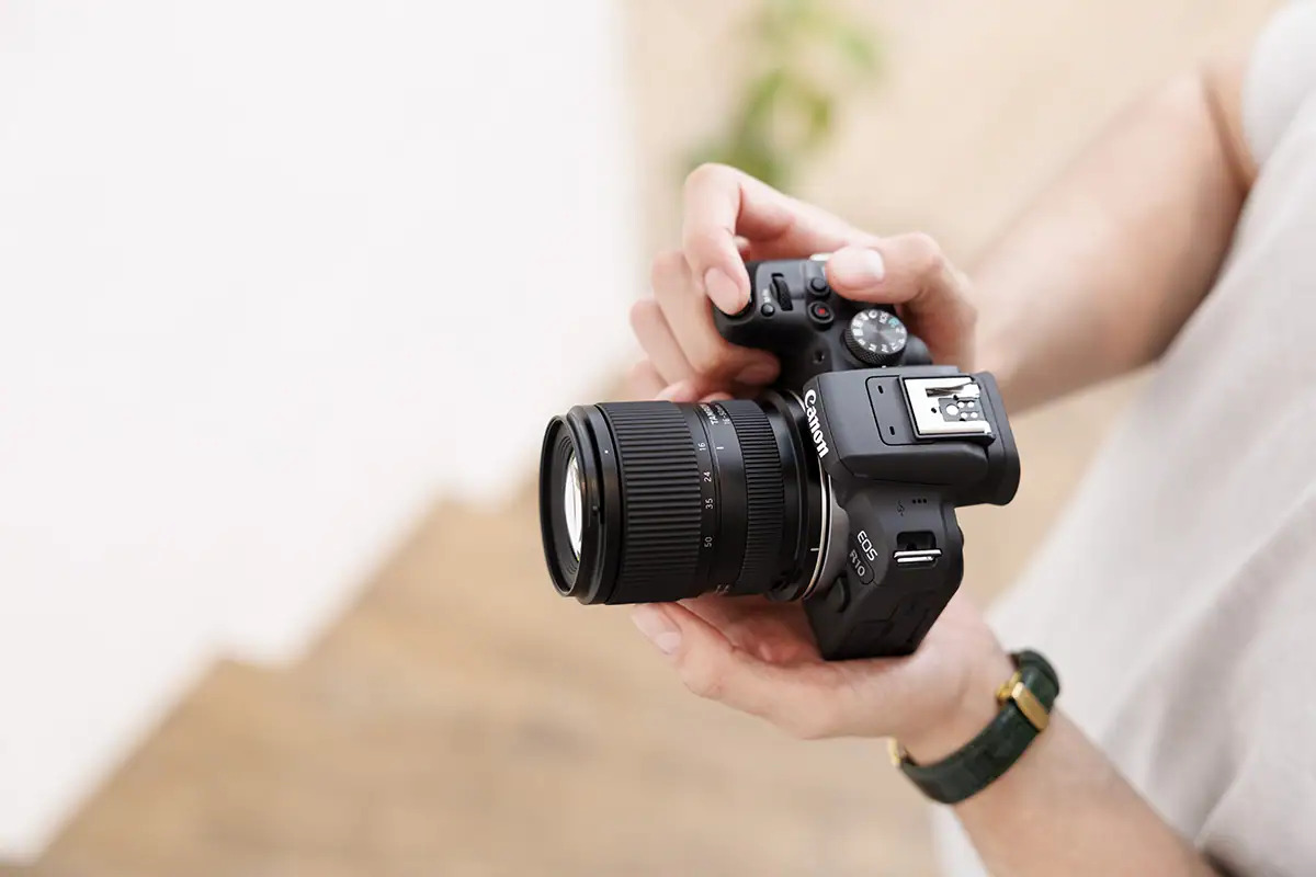 Canon EOS camera fitted with a Tamron 16-50mm f/2.8 zoom lens, held in a photographer's hands.