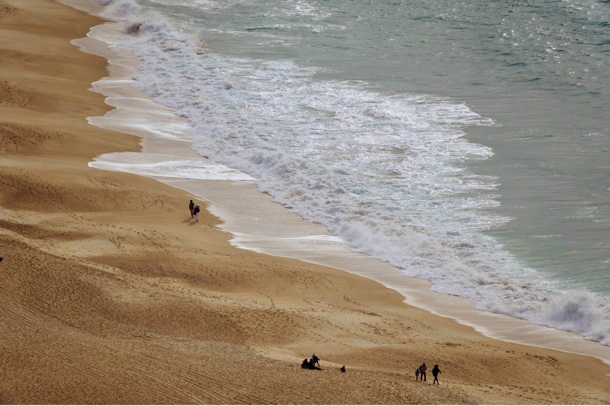Coastal beach landscape with ocean waves washing onto the sandy shore and people walking along the beach.