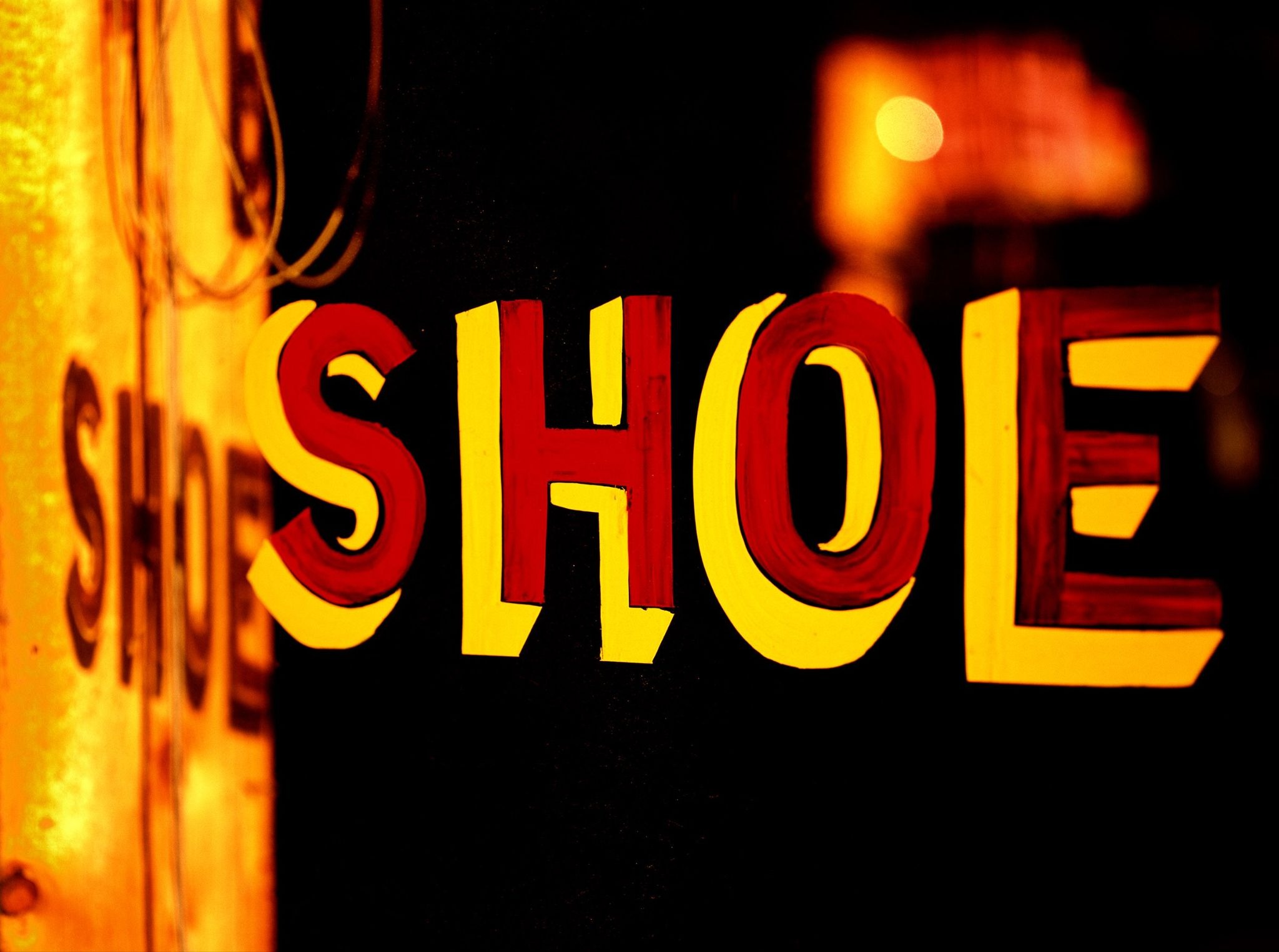 Illuminated yellow and red shoe shop sign against a dark background in Cedartown, Georgia, photographed by Stephen Wilkes.