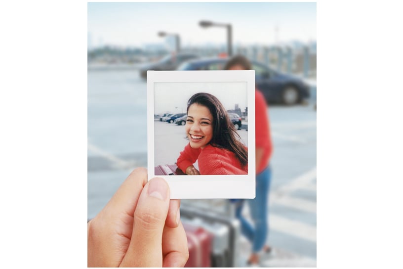 Hand holding an Instax instant photo with a person standing in the background